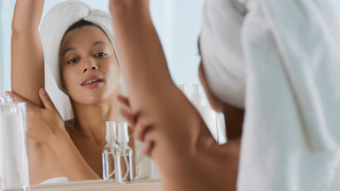 Woman raises arm and stokes it and armpit in front of the mirror