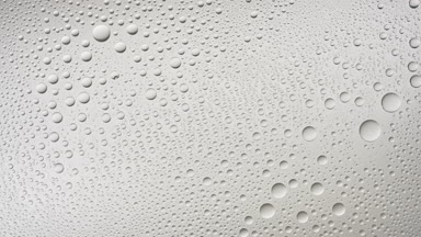Water drops blown off the wet glass surface on grey background