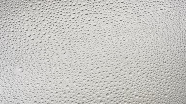 Water drops blown off the wet glass surface on grey background