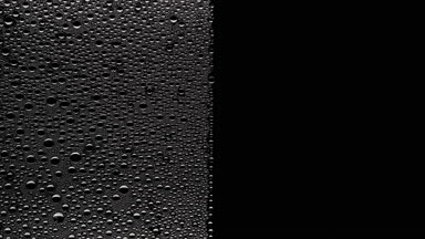 Water drops blown off the wet glass surface on black background