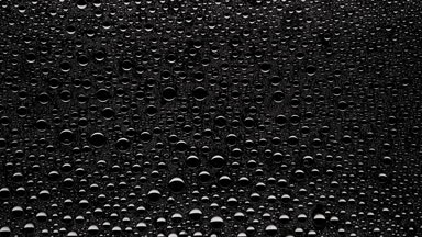 Water drops blown off the wet glass surface on black background