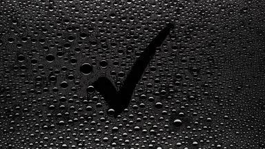 Checkmark sign blown off the wet glass on black background
