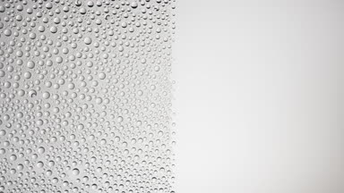 Big size water drops blown off the wet glass surface on grey bg