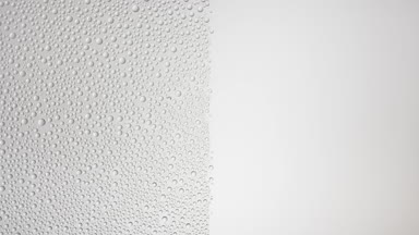 Medium size water drops blown off a wet glass surface on grey bg