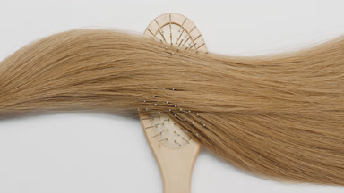 Lock of honey brown hair on brush comb on grey background