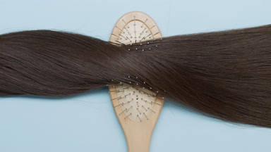 A Lock of brown hair on brush comb on pale blue background