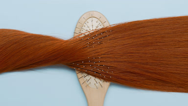 Lock of red hair on brush comb on pale blue background