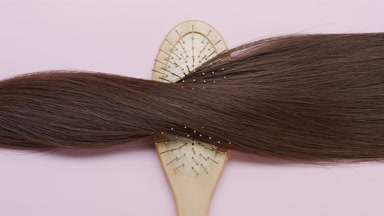 A Lock of brown hair on brush comb on pale pink background