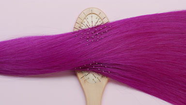 Lock of pink dyed hair on brush comb on pale pink background