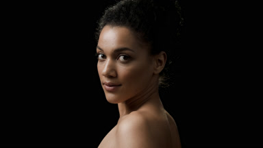 African brunette woman with curly hair in bun turns to camera