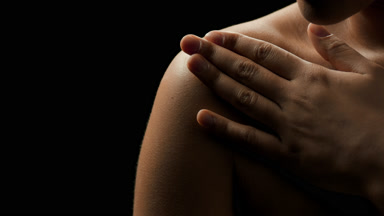 African female model with black curly hair strokes her clavicle