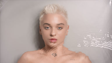 Woman opens eyes and looks at the camera through rippling water