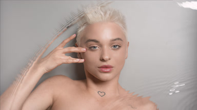 Woman strokes face under eye looking at the camera through water