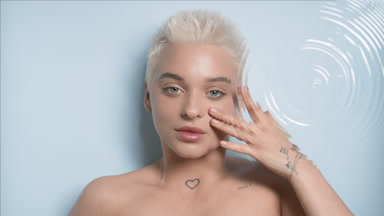 Blonde woman strokes her face under eye through rippling water