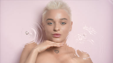 Young slim woman strokes jawline smiling through rippling water