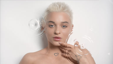Slim blonde woman strokes jawline smiling through rippling water