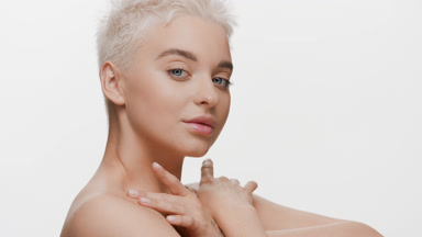 Slim blond woman with bare shoulders strokes collarbones turning