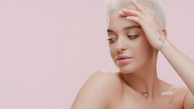 Cute young woman with bare shoulders strokes face turning head
