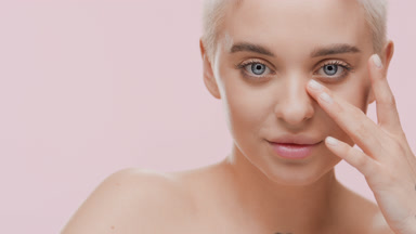 Attractive young blonde Caucasian woman strokes face under eye