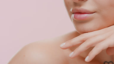 Caucasian woman with bare shoulder strokes her jawline smiling