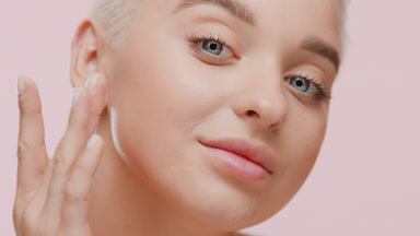 Fair-haired Caucasian woman touches cheek tapping and smiles