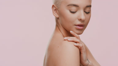 Pretty blond woman stokes shoulder and looks at camera smiling