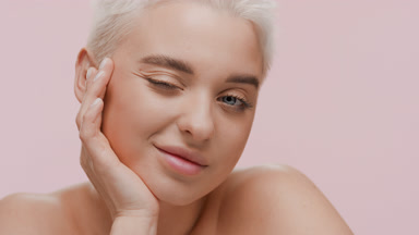 Blonde Caucasian woman winks at the camera resting head on hand