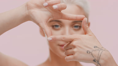 Pretty young blond Caucasian woman makes hand camera gesture