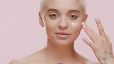 Beautiful Caucasian woman applies white cream on cheek smiling