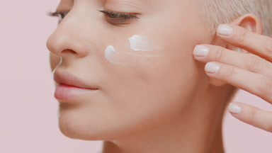 Woman puts moisturizer on cheek turning head from the camera