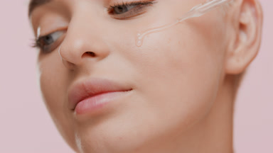 Pretty Caucasian woman drips clear serum from dropper on cheek