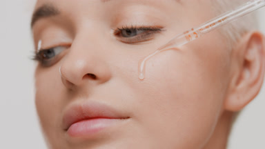 Caucasian woman drips transparent serum from dropper on cheek