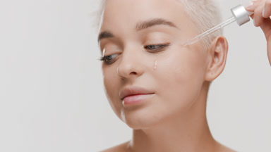 Woman drips serum from pipette on cheek and looks at the camera