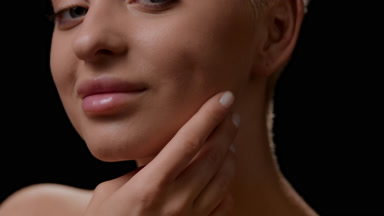 Caucasian woman strokes jawline looking at camera and smiling