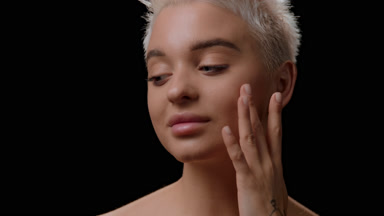 Young woman touches face tapping and looks at the camera smiling