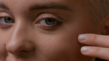 Caucasian woman strokes face under eye and looks at the camera