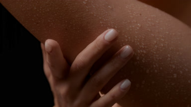 Macro shot of slim white-skinned woman strokes wet smooth arm