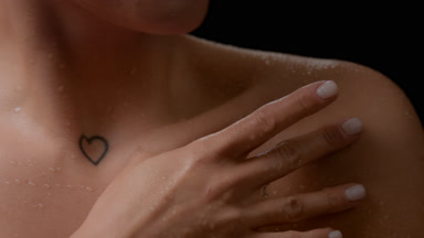 Macro of slim woman strokes her wet collarbones turning her head