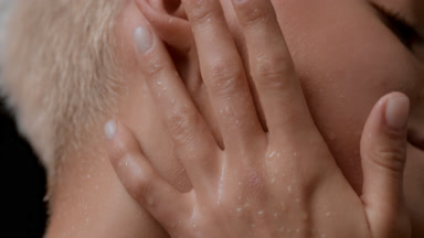 Macro shot of blond woman strokes her wet neck, face and ear