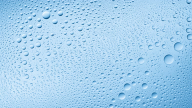 Water drops blown off the wet glass surface on blue background