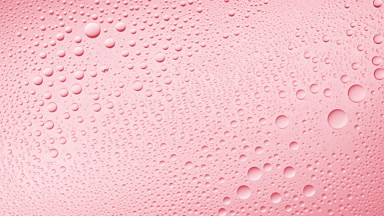 Water drops blown off the wet glass surface on pink background