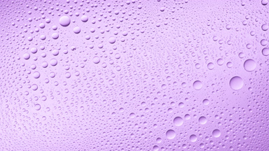 Water drops blown off the wet glass surface on purple background