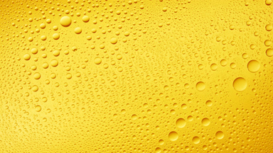 Water drops blown off the wet glass surface on yellow background