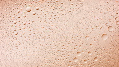 Water drops blown off the wet glass surface on beige background