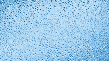 Water drops blown off the wet glass surface on blue background