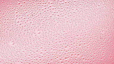 Water drops blown off the wet glass surface on pink background