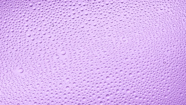 Water drops blown off the wet glass surface on purple background