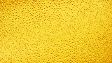 Water drops blown off the wet glass surface on yellow background