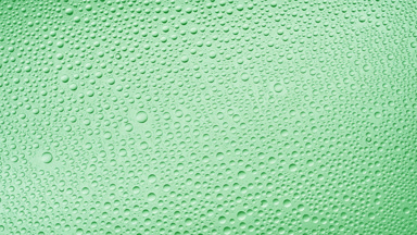 Water drops blown off the wet glass surface on green background