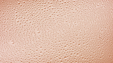 Water drops blown off the wet glass surface on beige background